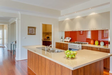 Mid-sized contemporary l-shaped open plan kitchen in Melbourne with a double-bowl sink, flat-panel cabinets, medium wood cabinets, granite benchtops, orange splashback, glass sheet splashback, stainless steel appliances, medium hardwood floors and with island.