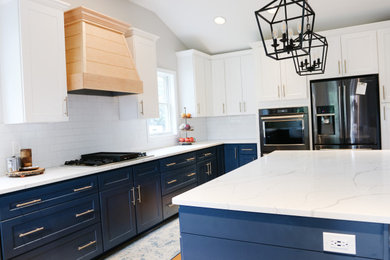 Large modern u-shaped kitchen/diner in Baltimore with a belfast sink, shaker cabinets, blue cabinets, engineered stone countertops, white splashback, metro tiled splashback, stainless steel appliances, medium hardwood flooring, an island, brown floors, white worktops and a vaulted ceiling.