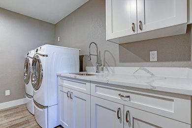 Ejemplo de lavadero contemporáneo con fregadero bajoencimera, puertas de armario blancas, encimera de mármol, suelo de madera clara, lavadora y secadora juntas, suelo marrón y encimeras blancas