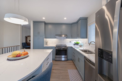 Inspiration for a mid-sized transitional l-shaped vinyl floor and brown floor enclosed kitchen remodel in Edmonton with a double-bowl sink, recessed-panel cabinets, blue cabinets, quartz countertops, white backsplash, ceramic backsplash, stainless steel appliances, an island and multicolored countertops