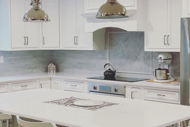 Inspiration for a large timeless l-shaped light wood floor and brown floor kitchen pantry remodel in Boston with a farmhouse sink, white cabinets, gray backsplash, ceramic backsplash, stainless steel appliances, an island, shaker cabinets and white countertops