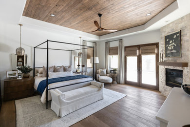 Inspiration for a transitional medium tone wood floor, brown floor, tray ceiling and wood ceiling bedroom remodel in Phoenix with white walls, a corner fireplace and a stone fireplace