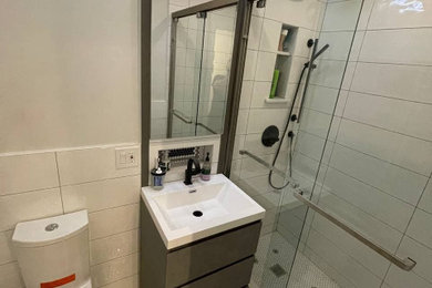 ニューヨークにあるお手頃価格の中くらいなコンテンポラリースタイルのおしゃれなバスルーム (浴槽なし) (アルコーブ型シャワー、一体型トイレ	、白いタイル、セラミックタイル、白い壁、モザイクタイル、オーバーカウンターシンク、白い床、引戸のシャワー、白い洗面カウンター、ニッチ、洗面台1つ、独立型洗面台) の写真