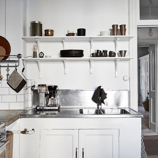 Bild på ett avskilt, litet skandinaviskt l-kök, med luckor med infälld panel, vita skåp och bänkskiva i rostfritt stål