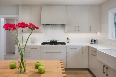Open concept kitchen - mid-sized farmhouse u-shaped light wood floor open concept kitchen idea in Portland with a farmhouse sink, flat-panel cabinets, light wood cabinets, quartz countertops, white backsplash, ceramic backsplash, stainless steel appliances, an island and white countertops