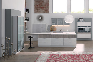 Inspiration for a large contemporary galley open plan kitchen in Leipzig with a drop-in sink, glass-front cabinets, light wood cabinets, solid surface benchtops, black appliances, laminate floors, a peninsula, white splashback and beige floor.