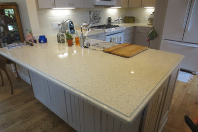 Eat-in kitchen - mid-sized traditional l-shaped dark wood floor eat-in kitchen idea in San Francisco with a farmhouse sink, raised-panel cabinets, white cabinets, quartz countertops, white backsplash, white appliances and a peninsula