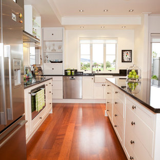 Transitional kitchen pantry inspiration - Example of a transitional medium tone wood floor kitchen pantry design in Hamilton with a double-bowl sink, white cabinets, granite countertops, white backsplash, stainless steel appliances and an island