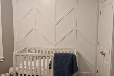 Ejemplo de habitación de bebé neutra actual de tamaño medio con paredes blancas, suelo de madera oscura, suelo marrón y boiserie