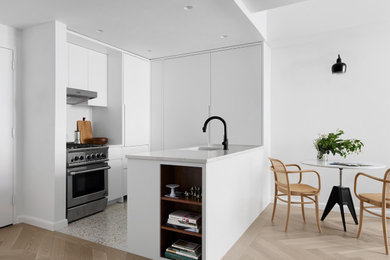 This is an example of a modern u-shaped eat-in kitchen in New York with an undermount sink, flat-panel cabinets, white cabinets, quartz benchtops, white splashback, stainless steel appliances, terrazzo floors, a peninsula, beige floor and white benchtop.