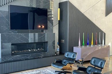 Diseño de salón abierto bohemio grande con paredes negras, suelo de madera en tonos medios, chimenea lineal, marco de chimenea de piedra, televisor colgado en la pared y suelo marrón