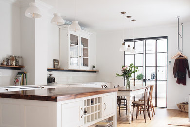 Mid-sized country single-wall light wood floor and brown floor eat-in kitchen photo in Montreal with an undermount sink, flat-panel cabinets, white cabinets, quartz countertops, white backsplash, paneled appliances, an island and white countertops