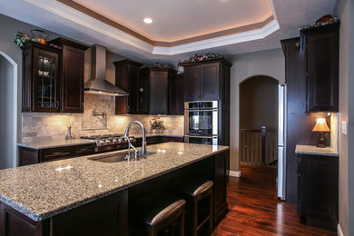 Large transitional single-wall dark wood floor enclosed kitchen photo in Other with an undermount sink, shaker cabinets, dark wood cabinets, granite countertops, beige backsplash, subway tile backsplash, stainless steel appliances and an island