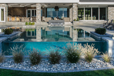 This is an example of a mid-sized traditional front yard rectangular infinity pool in Other with a water feature and natural stone pavers.