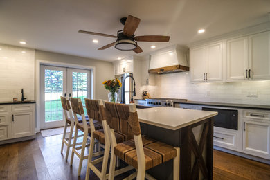 Mid-sized country galley eat-in kitchen in Philadelphia with a farmhouse sink, recessed-panel cabinets, white cabinets, soapstone benchtops, white splashback, subway tile splashback, stainless steel appliances, medium hardwood floors, with island, brown floor and black benchtop.