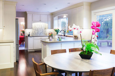 Example of a mid-sized transitional u-shaped brown floor and medium tone wood floor open concept kitchen design in San Francisco with an undermount sink, raised-panel cabinets, white cabinets, quartz countertops, beige backsplash, porcelain backsplash, stainless steel appliances and a peninsula