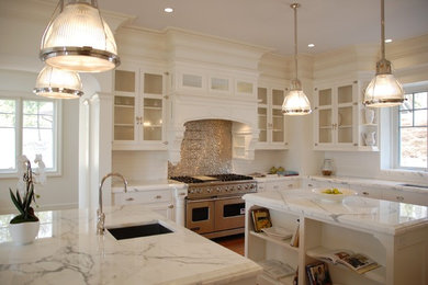 Photo of a large transitional u-shaped open plan kitchen in New York with an undermount sink, glass-front cabinets, white cabinets, marble benchtops, multi-coloured splashback, subway tile splashback, stainless steel appliances, medium hardwood floors, multiple islands, brown floor and white benchtop.
