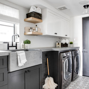 This is an example of a beach style single-wall separated utility room in Los Angeles with a belfast sink, shaker cabinets, grey cabinets, white walls, a side by side washer and dryer, multi-coloured floors and grey worktops.
