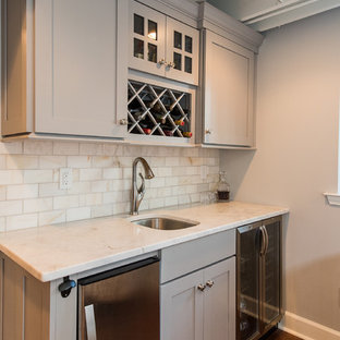 バーミングハムの中サイズのトラディショナルスタイルのおしゃれなウェットバー (アンダーカウンターシンク、シェーカースタイル扉のキャビネット、グレーのキャビネット、大理石カウンター、白いキッチンパネル、サブウェイタイルのキッチンパネル、濃色無垢フローリング) の写真