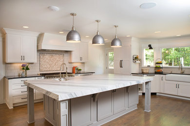 Kitchen pantry - large farmhouse medium tone wood floor kitchen pantry idea in Charlotte with a farmhouse sink, shaker cabinets, white cabinets, marble countertops, beige backsplash, ceramic backsplash, stainless steel appliances and an island
