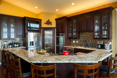 Kitchen pantry - traditional l-shaped medium tone wood floor kitchen pantry idea in Seattle with an undermount sink, raised-panel cabinets, dark wood cabinets, granite countertops, brown backsplash, mosaic tile backsplash, stainless steel appliances and an island