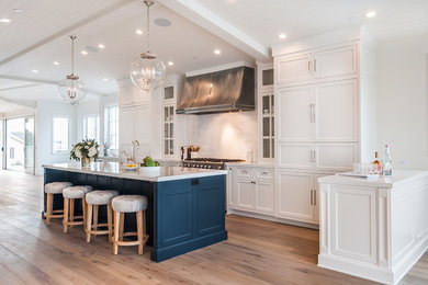Inspiration for a large country u-shaped open plan kitchen in Los Angeles with a farmhouse sink, recessed-panel cabinets, white cabinets, solid surface benchtops, white splashback, marble splashback, stainless steel appliances, light hardwood floors, with island, brown floor and white benchtop.