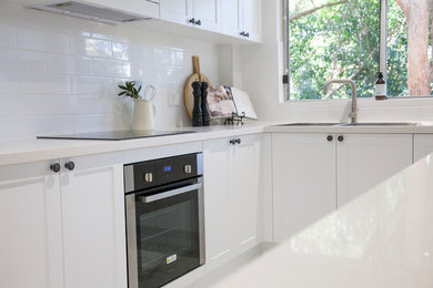 Design ideas for a mid-sized contemporary u-shaped separate kitchen in Sydney with a drop-in sink, shaker cabinets, white cabinets, quartz benchtops, white splashback, subway tile splashback, stainless steel appliances and porcelain floors.