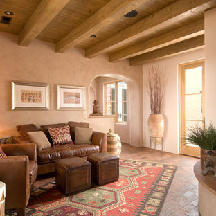 Mittelgroßes, Offenes, Repräsentatives, Fernseherloses Mediterranes Wohnzimmer mit Backsteinboden, Kaminsims aus Beton, beiger Wandfarbe, Eckkamin und braunem Boden in Albuquerque