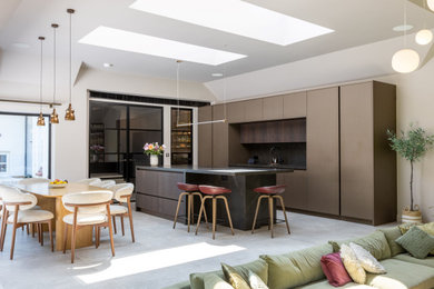 Photo of an expansive contemporary open plan kitchen in Manchester with a submerged sink, flat-panel cabinets, medium wood cabinets, engineered stone countertops, black splashback, black appliances, porcelain flooring, an island, grey floors, black worktops, a vaulted ceiling and feature lighting.