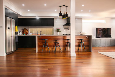 Large modern galley open plan kitchen in Wollongong with a double-bowl sink, flat-panel cabinets, black cabinets, quartz benchtops, grey splashback, stone slab splashback, stainless steel appliances, medium hardwood floors, with island and grey benchtop.