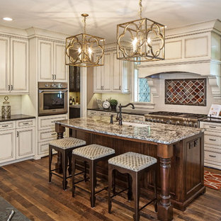 Diseño de cocina en L, tradicional renovada, de tamaño medio, abierta, con fregadero bajoencimera, puertas de armario blancas, encimera de granito, salpicadero blanco, electrodomésticos de acero inoxidable, suelo de madera oscura, una isla, armarios con rebordes decorativos y salpicadero de azulejos tipo metro