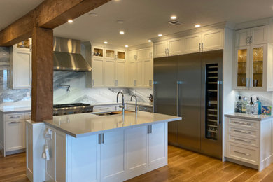Example of a large transitional l-shaped light wood floor and brown floor kitchen design in San Francisco with an undermount sink, shaker cabinets, white cabinets, quartz countertops, gray backsplash, marble backsplash, stainless steel appliances, an island and gray countertops