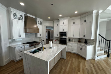 Large 1950s u-shaped light wood floor and yellow floor eat-in kitchen photo with an undermount sink, recessed-panel cabinets, white cabinets, quartzite countertops, white backsplash, stone slab backsplash, stainless steel appliances, an island and white countertops