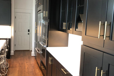 Example of a large trendy u-shaped medium tone wood floor and brown floor eat-in kitchen design in DC Metro with an undermount sink, recessed-panel cabinets, black cabinets, quartz countertops, white backsplash, quartz backsplash, stainless steel appliances, an island and white countertops
