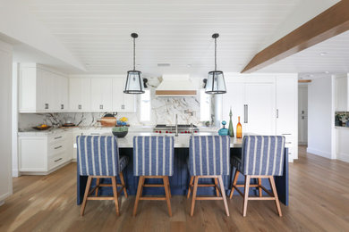 Example of a large beach style light wood floor kitchen design in Orange County with a farmhouse sink, shaker cabinets, white cabinets, marble countertops, paneled appliances and an island