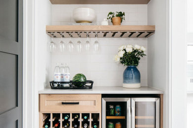 Imagen de bar en casa lineal pequeño sin pila con armarios estilo shaker, puertas de armario de madera clara, salpicadero blanco, suelo de madera clara y encimeras blancas