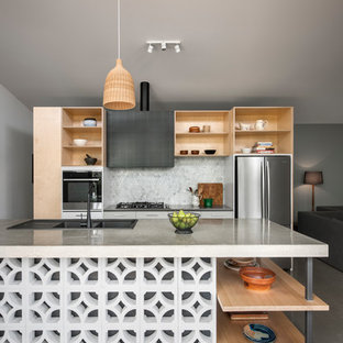 Imagen de cocina de galera, actual, abierta, con fregadero de doble seno, armarios abiertos, puertas de armario de madera clara, salpicadero verde, salpicadero con mosaicos de azulejos, electrodomésticos de acero inoxidable, suelo de cemento, una isla y suelo gris