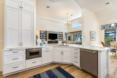 Large beach style l-shaped medium tone wood floor, brown floor and vaulted ceiling open concept kitchen photo in Miami with an undermount sink, shaker cabinets, white cabinets, quartz countertops, beige backsplash, subway tile backsplash, stainless steel appliances, a peninsula and multicolored countertops