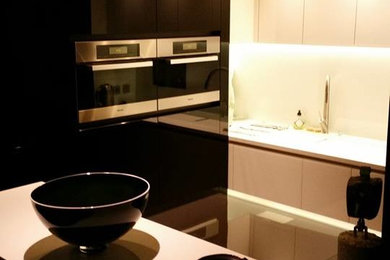 Idées déco pour une petite cuisine contemporaine en U fermée avec un évier intégré, un placard à porte affleurante, des portes de placard noires, un plan de travail en surface solide, une crédence blanche, une crédence en feuille de verre, un électroménager noir, sol en béton ciré, îlot, un sol gris et un plan de travail blanc.