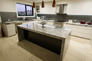 Large modern l-shaped kitchen pantry in Melbourne with a drop-in sink, beaded inset cabinets, white cabinets, glass sheet splashback, stainless steel appliances, ceramic floors and with island.