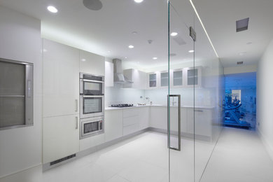 Photo of a mid-sized contemporary kitchen in London with an undermount sink, flat-panel cabinets, white cabinets, solid surface benchtops, white splashback, glass sheet splashback, stainless steel appliances and porcelain floors.