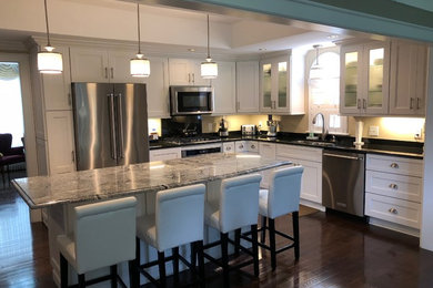 Eat-in kitchen - large transitional l-shaped medium tone wood floor and brown floor eat-in kitchen idea in New York with a double-bowl sink, shaker cabinets, white cabinets, granite countertops, beige backsplash, stainless steel appliances, an island and black countertops