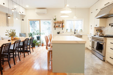 Photo of a mid-sized transitional u-shaped eat-in kitchen in New York with a farmhouse sink, recessed-panel cabinets, white cabinets, quartzite benchtops, white splashback, ceramic splashback, stainless steel appliances, medium hardwood floors, with island, multi-coloured floor and white benchtop.