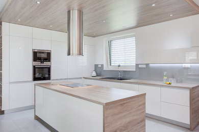 Kitchen - contemporary l-shaped kitchen idea in Other with a drop-in sink, flat-panel cabinets, white cabinets, wood countertops, gray backsplash, stainless steel appliances and an island