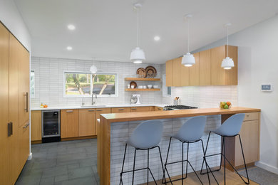 This is an example of a medium sized retro u-shaped kitchen/diner in Philadelphia with a submerged sink, flat-panel cabinets, light wood cabinets, engineered stone countertops, white splashback, ceramic splashback, integrated appliances, slate flooring, an island, green floors and white worktops.