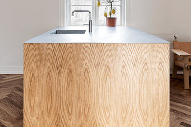 This is an example of a contemporary kitchen in Copenhagen with a drop-in sink, flat-panel cabinets, light wood cabinets, medium hardwood floors and with island.