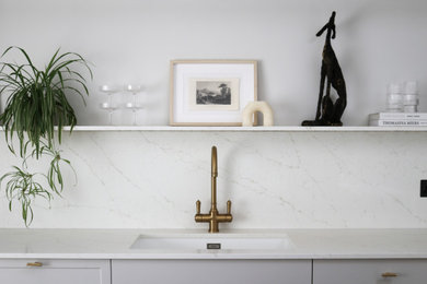 Inspiration for a large scandinavian single-wall kitchen/diner in Edinburgh with a single-bowl sink, shaker cabinets, beige cabinets, quartz worktops, white splashback, engineered quartz splashback, black appliances, light hardwood flooring, an island, beige floors and white worktops.