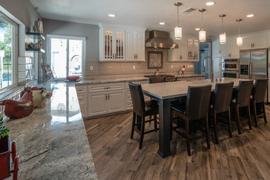 Example of a classic ceramic tile and brown floor eat-in kitchen design in Los Angeles with a farmhouse sink, raised-panel cabinets, white cabinets, granite countertops, gray backsplash, ceramic backsplash, stainless steel appliances and gray countertops