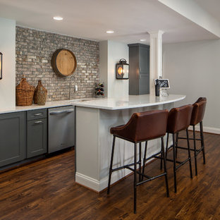 ワシントンD.C.のトランジショナルスタイルのおしゃれな着席型バー (アンダーカウンターシンク、シェーカースタイル扉のキャビネット、グレーのキャビネット、レンガのキッチンパネル、茶色い床、白いキッチンカウンター、ラミネートの床) の写真
