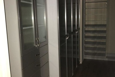 Example of a mid-sized transitional gender-neutral dark wood floor and brown floor walk-in closet design in Louisville with glass-front cabinets